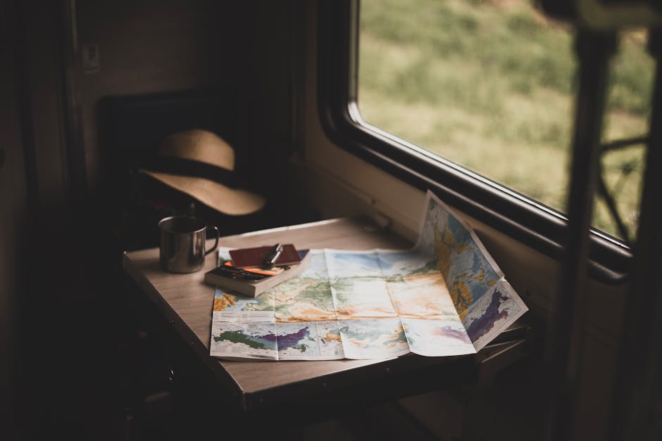 A serene train ride setup with a world map, mug, and hat on a table, suggesting stress free travel plans.